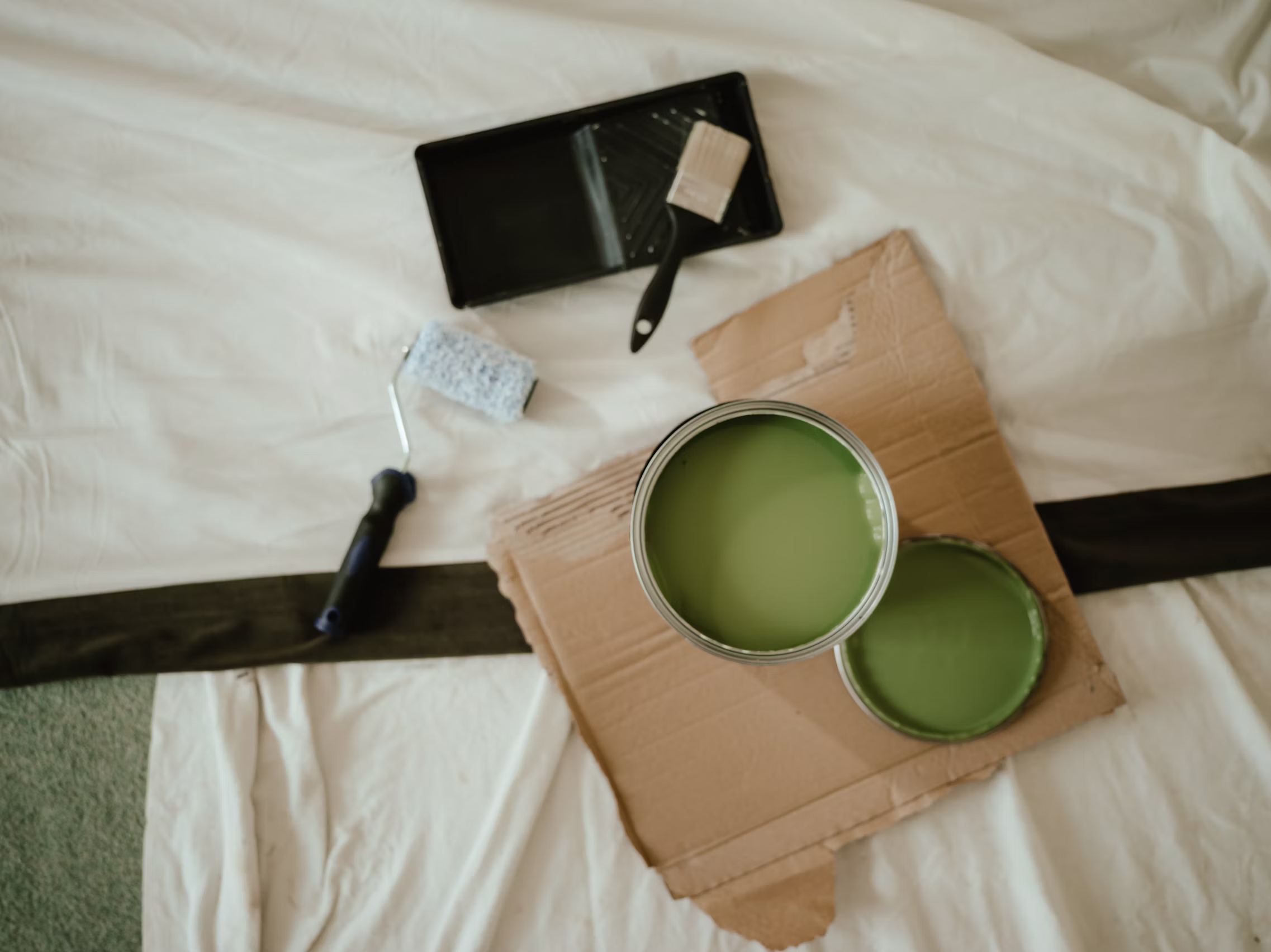 Sage-green paint, a roller, and tray laid out on a drop cloth, ready for the next coat